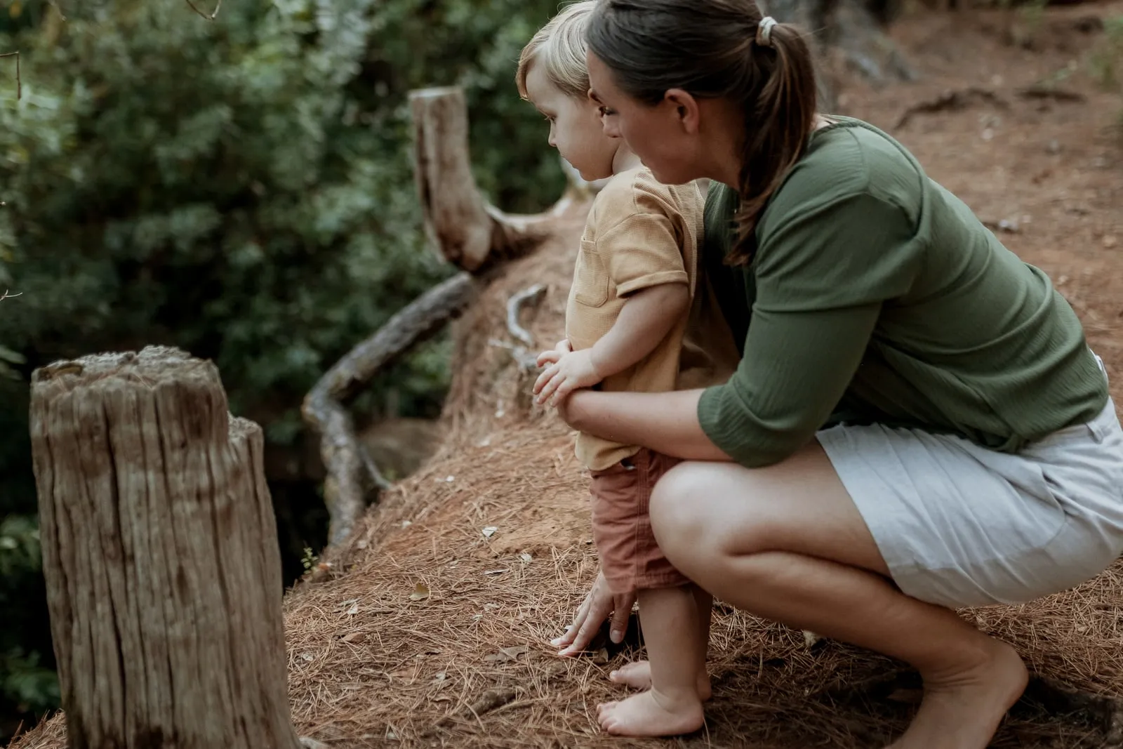 Eine Mutter hockt neben ihrem kleinen Sohn im Wald, beide schauen in dieselbe Richtung